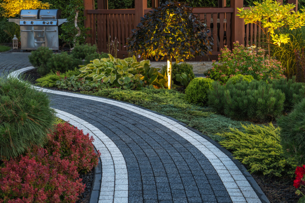 Concrete paver pathway through garden with outdoor lighting.